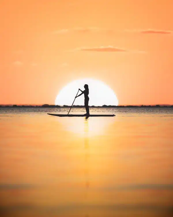 Jensen Beach - Paddleboard Sunset - Outdoor Activities Image courtesy of the Martin County Office of Tourism shows a beautiful sunset in Jensen Beach in the background while a person enjoys paddleboarding the Indian River Lagoon
